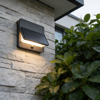 Solar wall light fixture on a stone wall with greenery in the foreground