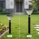 A split-screen comparison of a black solar garden stake light on a green lawn, showing two heights: 50 cm on the left and 75 cm on the right. The light features a ribbed clear shade and a black pole and base, with blurred houses in the background.