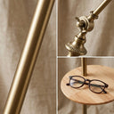 FL068 lamp detail close-ups: brushed gold electroplated pole, precision butterfly adjustment knob at the arc joint, and smooth natural wood tray with a pair of reading glasses