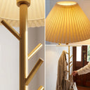 Close-up of gold floor lamp details: metal pole with coat hooks, pleated fabric shade texture, hanging coat and bag, modern design for entryway or bedroom storage lighting