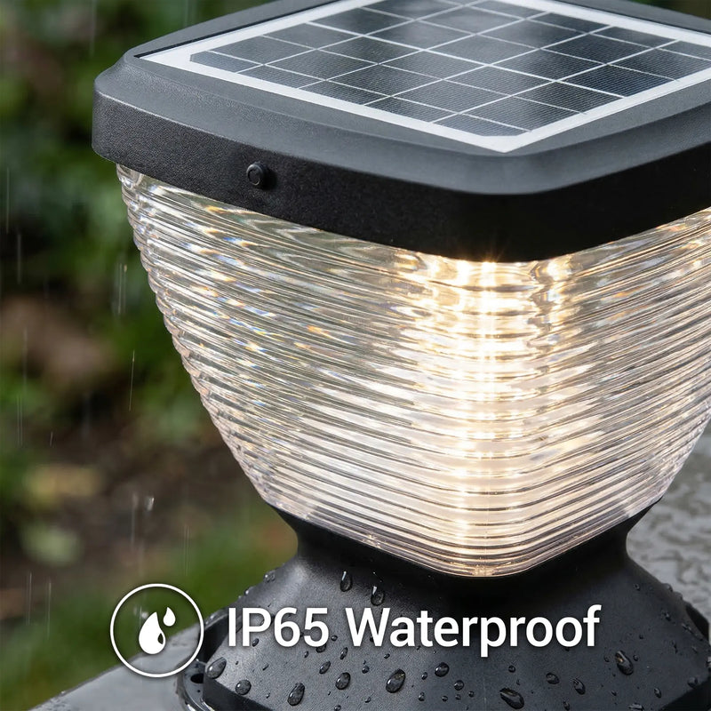 Close-up of Nexi Solar Pillar Light PT0112 ribbed clear dome glowing warm white in rainfall, 5W monocrystalline solar panel on top, water droplets on base, IP65 Waterproof icon overlay
