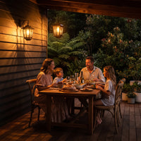 Family of four enjoying dinner on wooden deck under HeritageGlow Solar Lanterns mounted on wall and hanging from pergola, showcasing their use as ambient outdoor dining lighting that enhances family gatherings with warm, inviting glow.