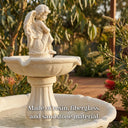 Close-up of OUTWAY angel solar garden fountain upper tier showing cream yellow winged angel statue and scalloped basin in an Australian native garden with bottlebrush and eucalyptus with text overlay Made of resin fiberglass and sandstone material