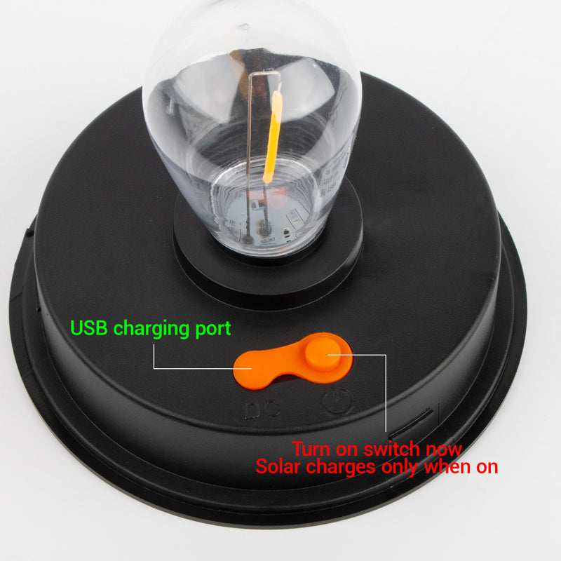 A black circular solar light base with a clear bulb on top, featuring an orange power switch and text labels pointing to the USB charging port and power switch.