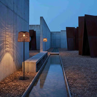 Two rattan solar lamps along concrete water feature in modern courtyard at dusk.