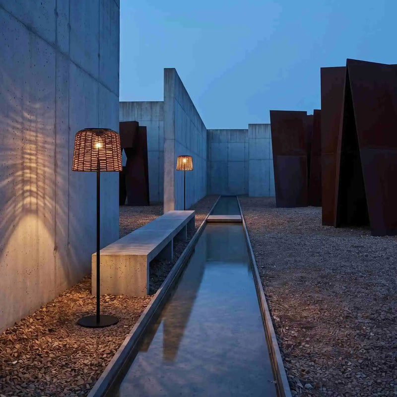 Two rattan solar lamps along concrete water feature in modern courtyard at dusk.