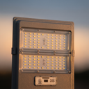 A close-up of a rectangular outdoor LED street light with two illuminated light panels and a small control label reading 'Radar Sensor' on a warm sunset background.