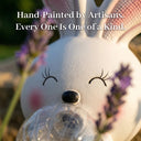 Extreme close-up of OUTWAY Hoppi A004 sitting solar bubble rabbit face showing hand-painted matte resin detail eyelashes pink cheeks and clear solar bubble lantern in mouth surrounded by lavender with text overlay Hand-Painted by Artisans Every One Is One of a Kind