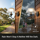 A split promotional image showing a wall-mounted outdoor light fixture in two settings: a sunny backyard deck scene on the left and a rainy porch scene on the right. The fixture has a ribbed white shade, warm glowing bulb, and dark metal mount.