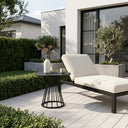 Modern outdoor lounge chair with a small table on a wooden deck, surrounded by greenery.