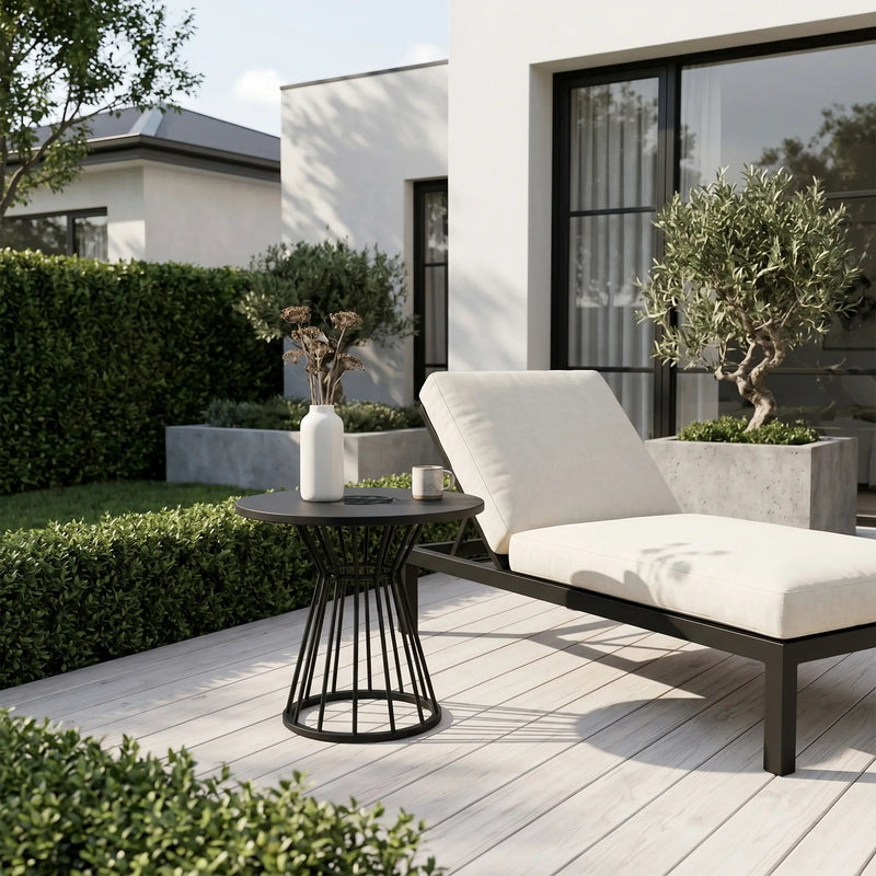 Modern outdoor lounge chair with a small table on a wooden deck, surrounded by greenery.