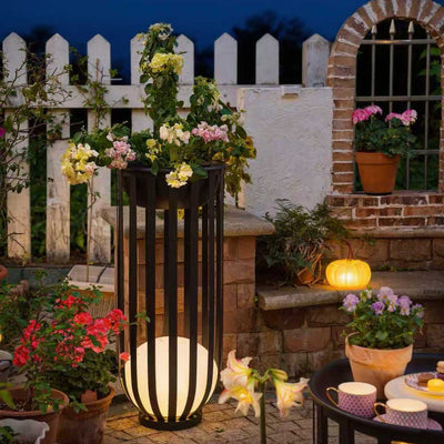 A garden setting showcasing a vase of flowers next to a solar floor lamp with table.