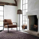 Wicker floor lamp beside leather chair and fireplace in bright loft-style room.