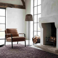 Wicker floor lamp beside leather chair and fireplace in bright loft-style room.