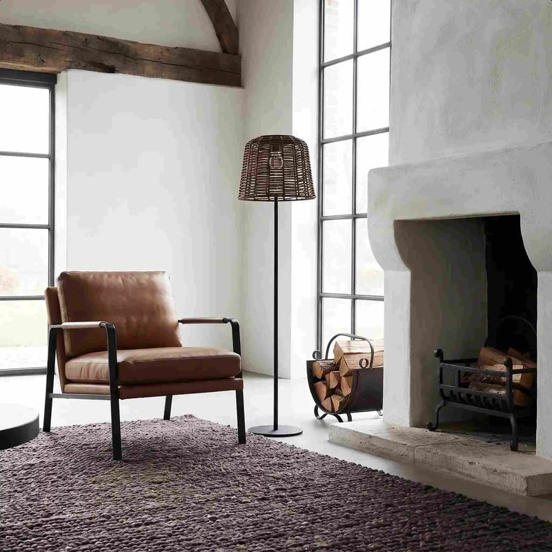 Wicker floor lamp beside leather chair and fireplace in bright loft-style room.