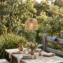 PT0913 solar rattan pendant over rustic wooden table with native flowers and ceramic tableware — solar panel mounted on fence rail, showcasing natural outdoor integration and warm 3000K glow for garden dining.