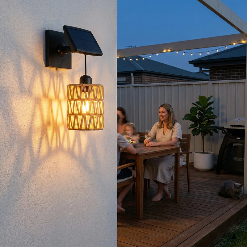 PT0909 solar wall sconce mounted on white stucco wall at dusk, casting warm woven shadow patterns beside wooden dining table where family enjoys wine — cozy alfresco ambiance with IP54 rating and dual solar/USB power.