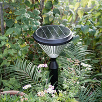 Solar pillar light in a natural setting with greenery and flowers