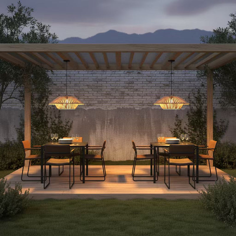 A dining area under a pergola, complete with chairs and a table, highlighted by a solar handwoven bamboo ceiling light.