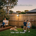 Australian family backyard at dusk — mother relaxing with wine, two children playing soccer, golden retriever on the lawn, PT0711 Cube solar wall light mounted on timber fence. Text: "Light up your night without the glare. Solar. Soft. Simple."