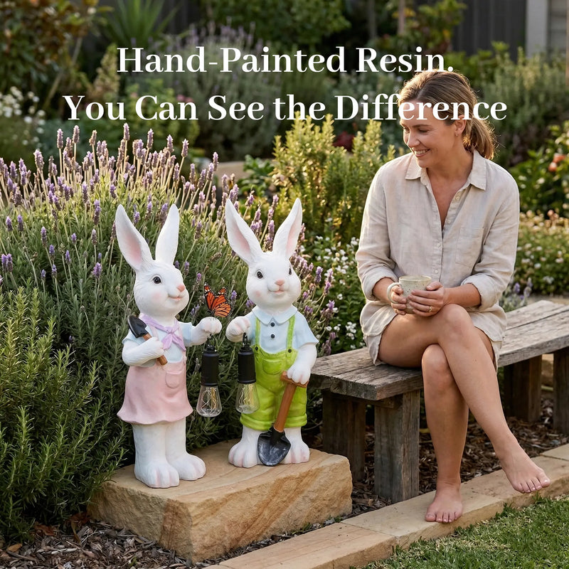 A woman sitting on a wooden bench in a lavender garden smiling at two hand-painted white resin rabbit garden ornaments holding solar lanterns, with text overlay Hand-Painted Resin You Can See the Difference