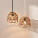 Two woven rattan pendant lights with black cords and exposed bulbs, hanging against a warm off-white wall with soft shadows.