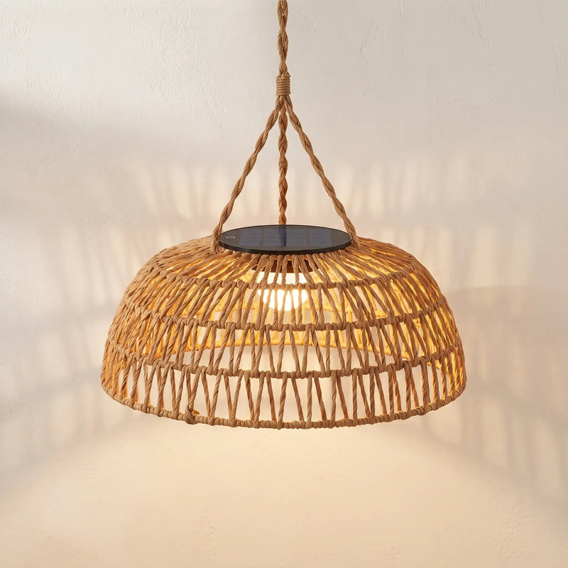 A dome-shaped woven rattan pendant light with a warm glowing light inside, suspended by a thick rope from a black circular top plate against a textured off-white wall.