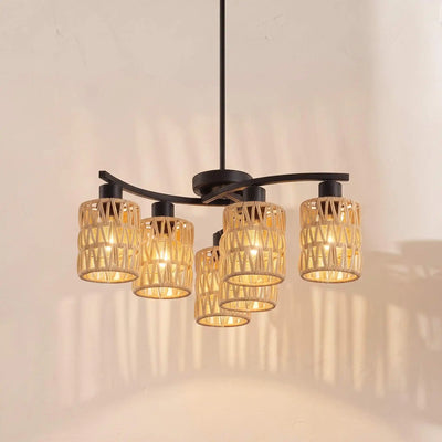 A modern five-light chandelier with a matte black metal frame and cylindrical woven rattan shades, glowing with warm yellow light against a textured beige wall.