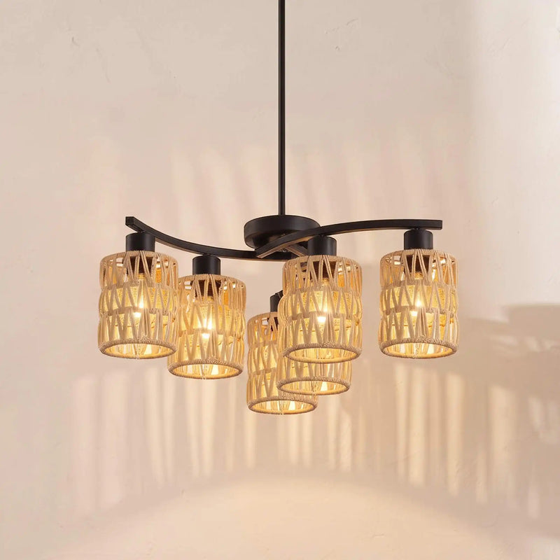 A modern five-light chandelier with a matte black metal frame and cylindrical woven rattan shades, glowing with warm yellow light against a textured beige wall.