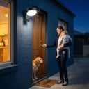 Serra solar wall light mounted above front door number 24, mother holding sleeping child unlocking door at night with golden retriever