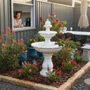 OUTWAY F001 ivory white two-tier solar garden fountain in an Australian native garden with rainbow lorikeets drinking from the lower basin surrounded by red bottlebrush while a woman smiles from a kitchen window with a coffee mug