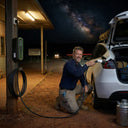 Man charging a car at a gas station under a starry night sky.