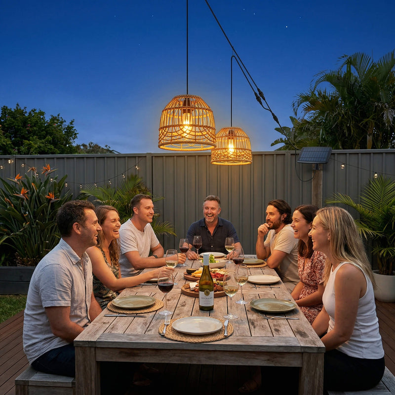 Group of people enjoying a meal outdoors at night with string lights.