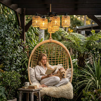Woman reading a book with a dog on her lap in a hanging chair surrounded by plants.