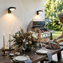 Two Serra solar wall lights mounted on marble wall illuminating elegant outdoor dining table set with native Australian flowers and candles
