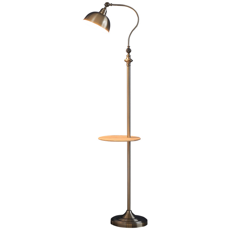 A vintage-style floor lamp with a curved brass neck, adjustable dome shade, and a small round wooden shelf on a solid white background.