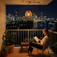 Woman reading book on balcony under PT0913 pendant with city skyline view — serene urban retreat vibe with gentle pulse mode and USB backup power for cloudy days, ideal for quiet nights.