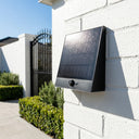 Solar-powered outdoor light fixture attached to a white brick wall.