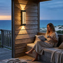 Woman reading a book on a wooden deck with ocean view at night.