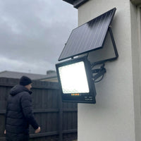 Solar-powered outdoor light fixture on a wall with a person in the background.