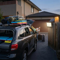 Car with roof rack and surfboards, family with suitcases in driveway
