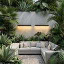 Solar Wall Lights glowing warm amber 3000K on grey rendered feature wall, set in lush tropical outdoor living space with L-shaped sectional sofa, monstera and palm plants, stone paver patio