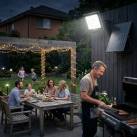 Family gathered around a table in a backyard with a solar light fixture and grill.