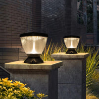 Two outdoor solar pillar light on stone plinths with a brick wall and plants in the background.