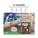An outdoor product demonstration showing a portable power station branded URANI on the ground next to a person using a chainsaw to cut a log. The power station is orange and black with a built-in handle and multiple output ports, including a power cord plugged in.