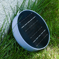 Round solar garden light with panel resting on grass beside stone wall