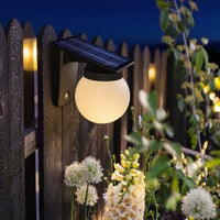 Solar Upside Down Planet Wall Light fixture on a wooden fence with flowers in the foreground.