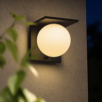 Modern outdoor solar wall light fixture on a textured wall with a plant in the foreground.