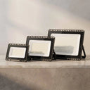 Three black rectangular LED floodlights in different sizes arranged on a light gray stone surface against a soft gray background.