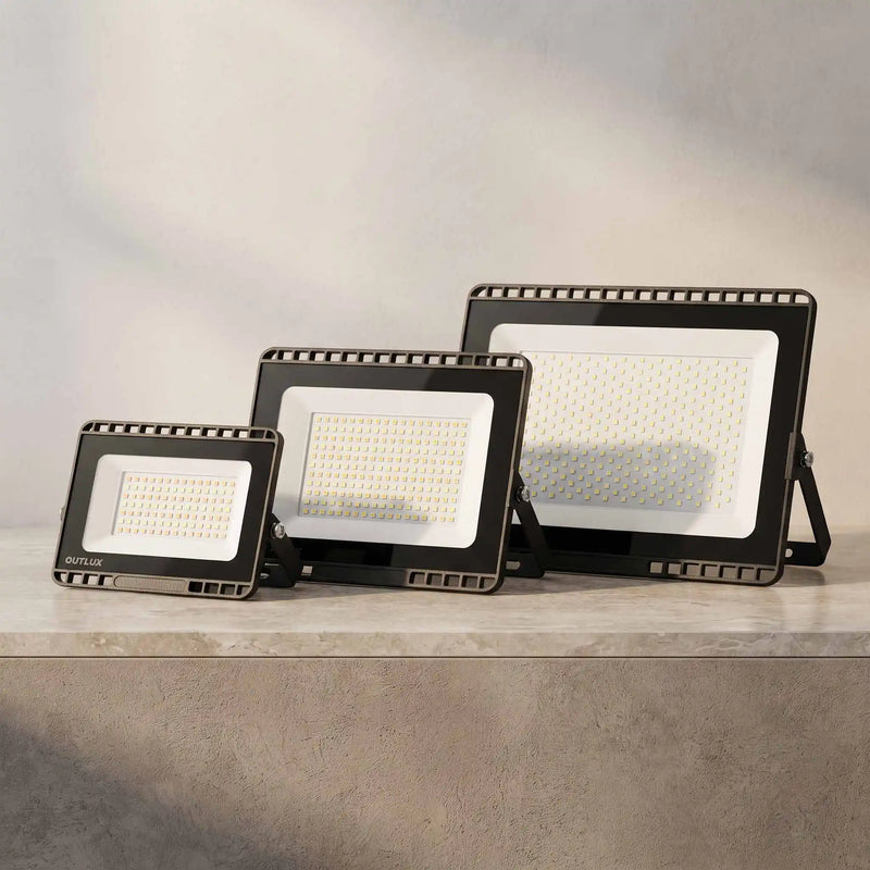 Three black rectangular LED floodlights in different sizes arranged on a light gray stone surface against a soft gray background.